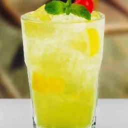 Szklanka z zielonym napojem, kostkami lodu, plasterkami cytryny, udekorowana wiśnią koktajlową i listkami mięty.